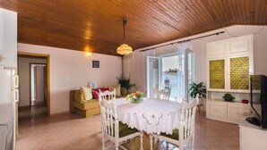 Un coin repas avec un plafond en bois, une table ronde entourée de chaises blanches et une vue dégagée sur l’extérieur grâce à une porte ouverte.