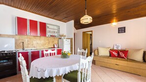 Une cuisine avec des meubles de rangement rouges, un réfrigérateur blanc et une table à manger avec des chaises blanches.