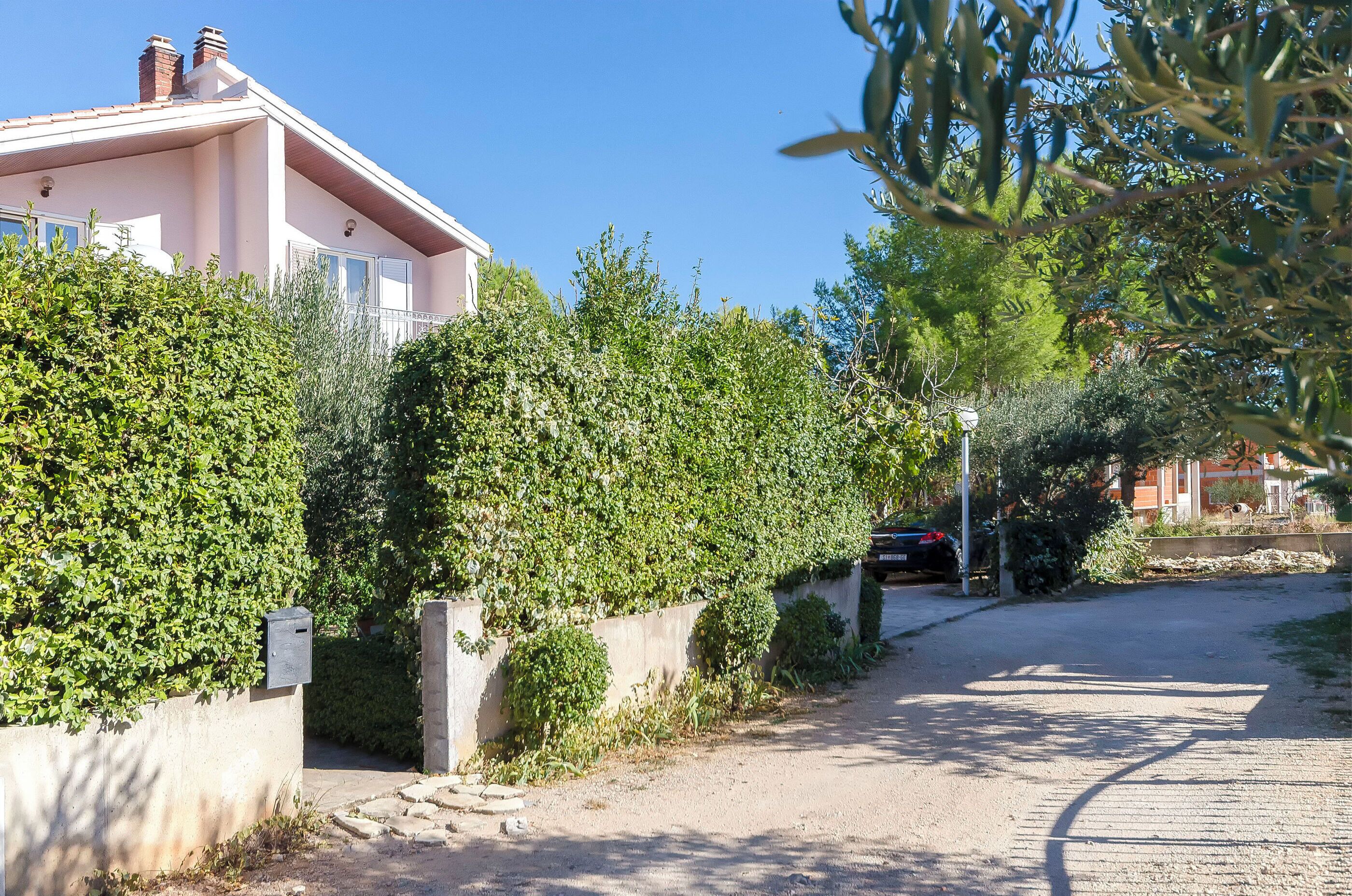 Una calle residencial con una casa rosa, abundante vegetación y un coche estacionado.