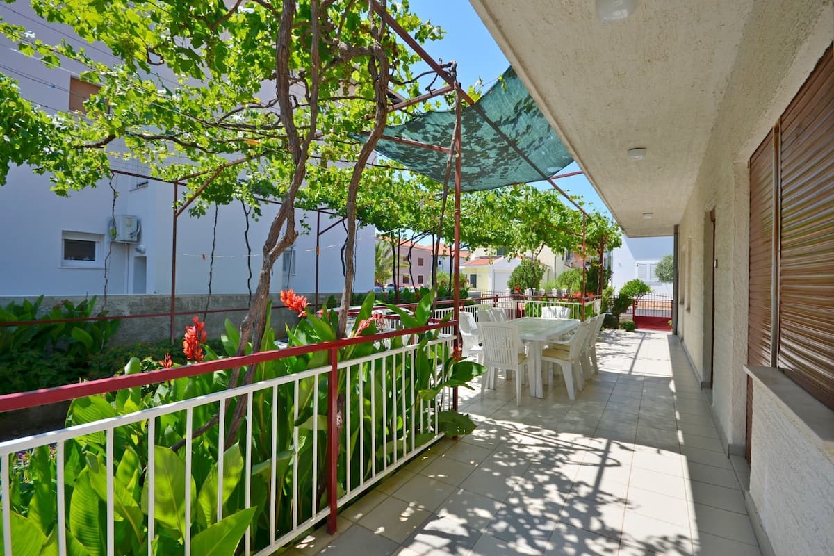 A balcony with a table and chairs, surrounded by greenery and a red railing.