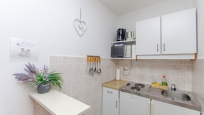 A small kitchenette with white cabinets, a sink, and a countertop. There is a heart-shaped decoration on the wall and a sign with a welcome message. - Apartments Cosic (Igrane)