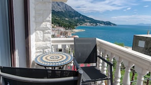A balcony with a view of a coastal town, a tiled table, and two chairs. - Apartments Cosic (Igrane)