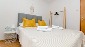 A neatly made bed with striped bedding, two yellow pillows, and a white lamp on a bedside table. - Apartments Cosic (Igrane)