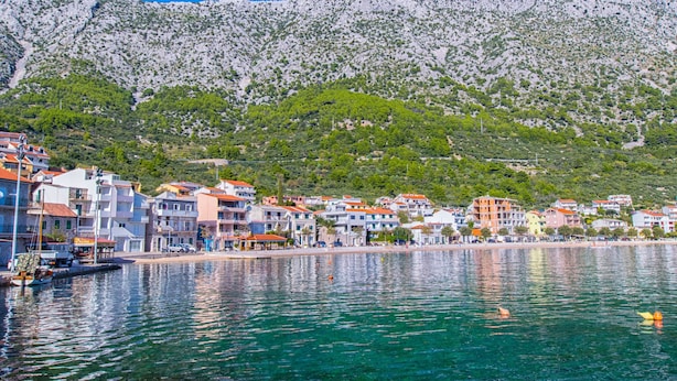 A coastal town with buildings along the waterfront, a clear blue sky, and a mountain in the background. - Apartments Cosic (Igrane)