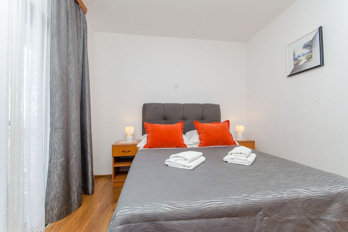 Un lit bien fait, recouvert d’une couvre-lit à motifs gris et blancs, avec deux oreillers orange et deux serviettes blanches pliées sur le lit.