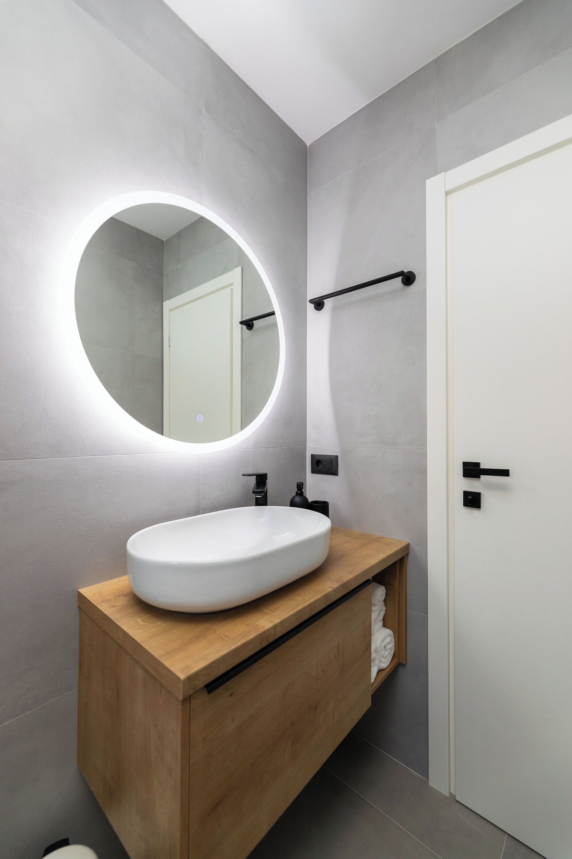 A modern bathroom with a round mirror, a white sink, and a wooden vanity.