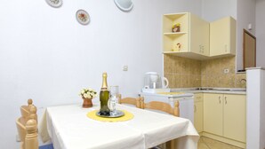 A small kitchen with a dining table set for two, a coffee maker, and a bottle of champagne. - Apartment Smiljana (Omis)