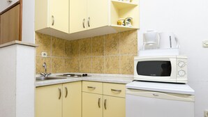 A compact kitchen with yellow cabinets, a white microwave, and a coffee maker. - Apartment Smiljana (Omis)