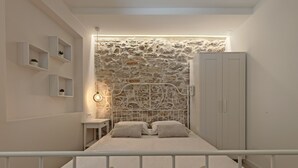 A bedroom with a stone wall, a bed with two pillows, a bedside table, and a wardrobe. - Apartments Mateo (Vodice)