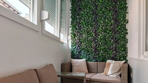 A corner seating area with a woven sofa and cushions, a glass table, and a wall covered with green foliage. - Apartments Mateo (Vodice)