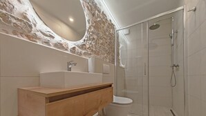 A modern bathroom with a stone wall, a wooden vanity, a white sink, a toilet, and a glass-enclosed shower. - Apartments Mateo (Vodice)