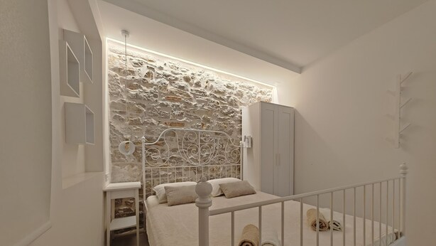 A bedroom with a stone wall, a bed with a white frame, a wardrobe, and a small bedside table. - Apartments Mateo (Vodice)
