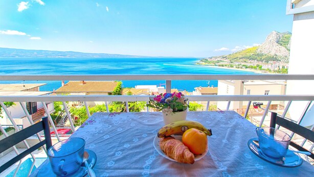 A balcony with a table set for breakfast, overlooking a coastal view. - Apartments Tomislav (Omis)