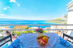 A balcony with a table set for breakfast, overlooking a coastal view. - Apartments Tomislav (Omis)