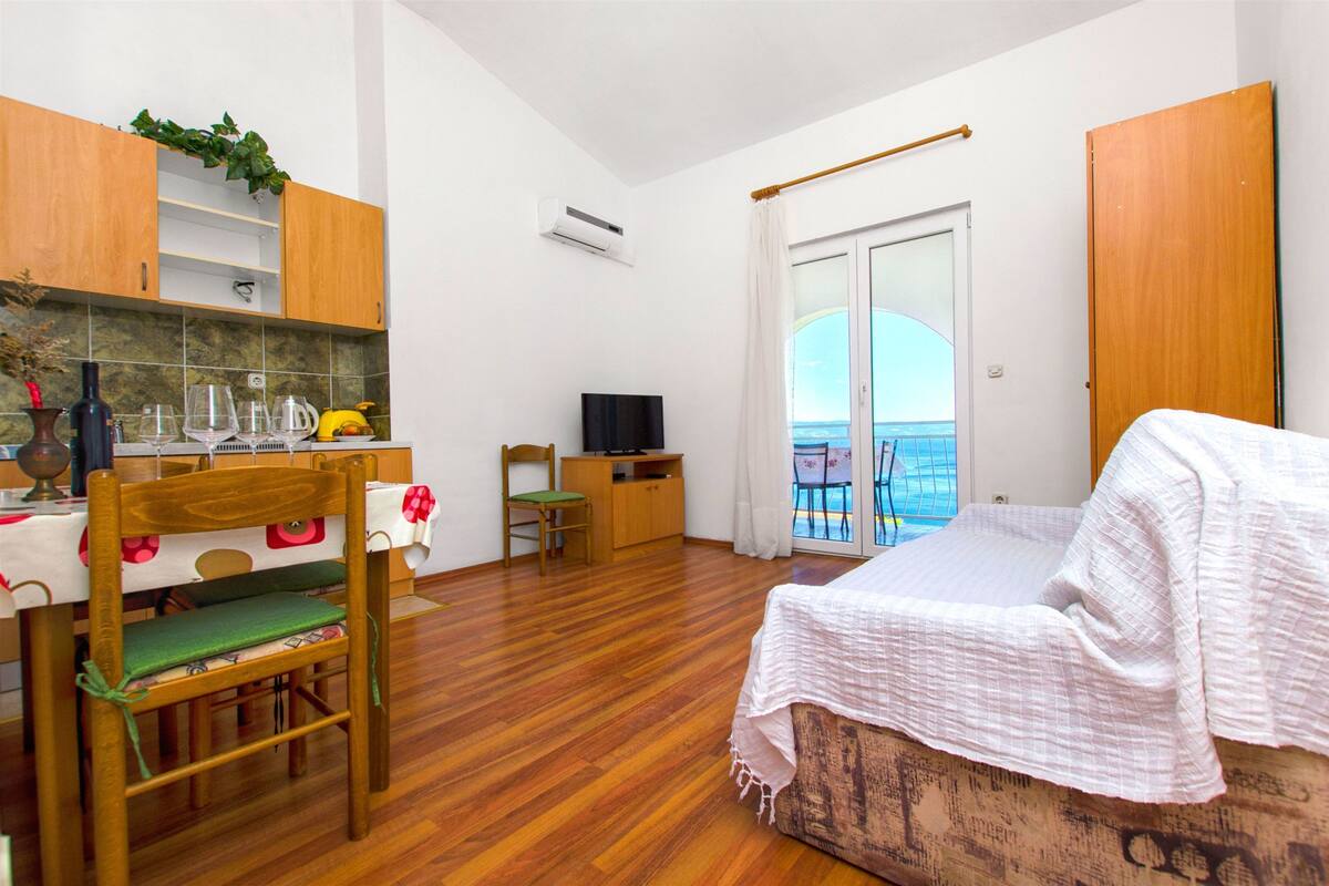 A room with a bed, a dining table, a TV, and a view of the sea.