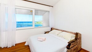 A bedroom with a large window, a wooden headboard, and a neatly made bed with towels. - Apartments Tomislav (Omis)