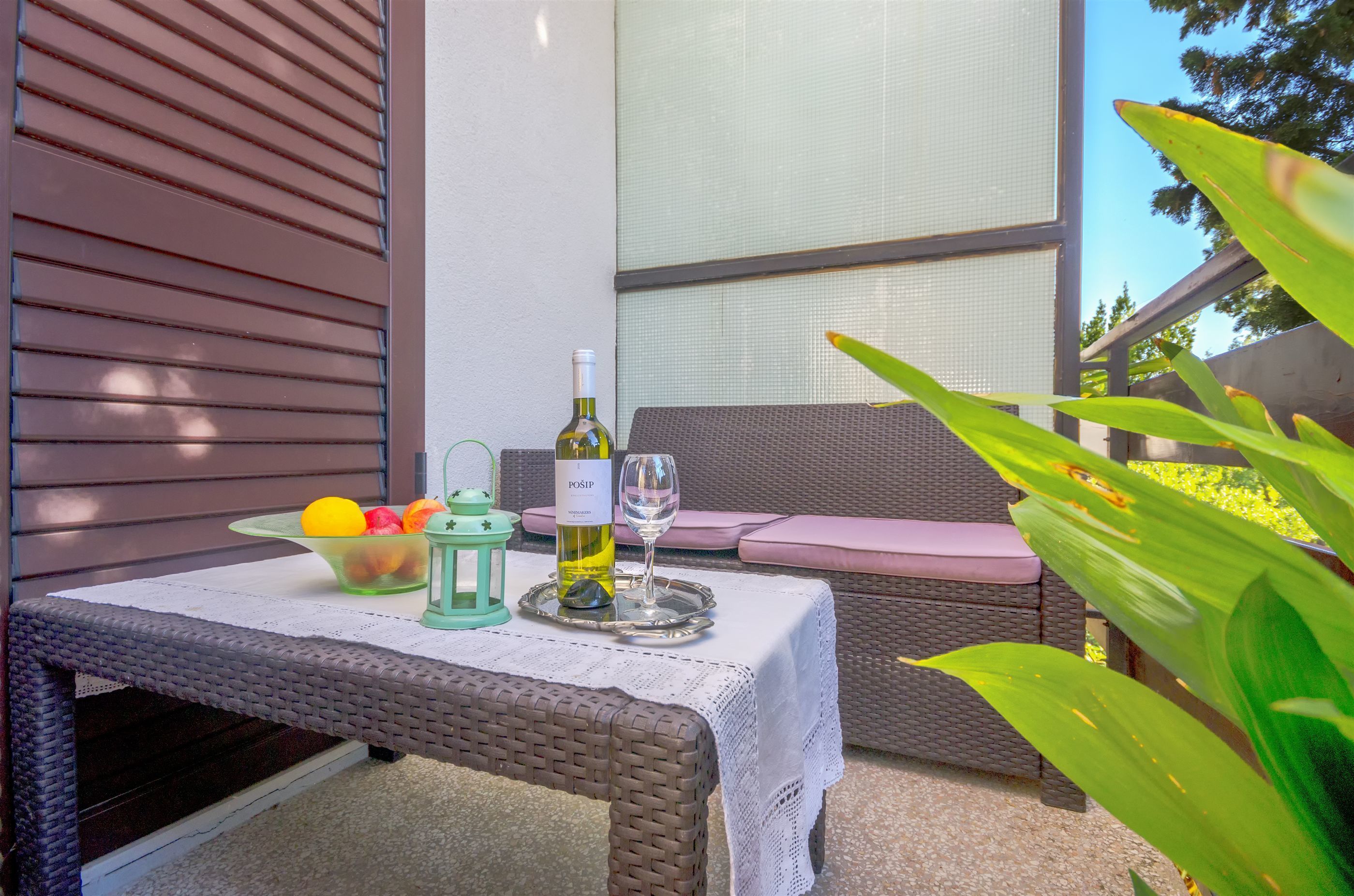 A wicker table with a bottle of wine, a glass, and a bowl of fruit.