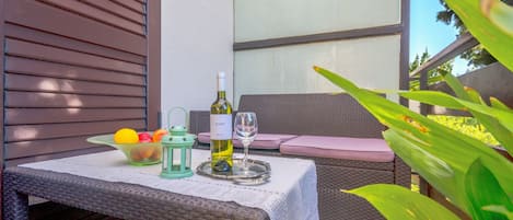 A wicker table with a bottle of wine, a glass, and a bowl of fruit.