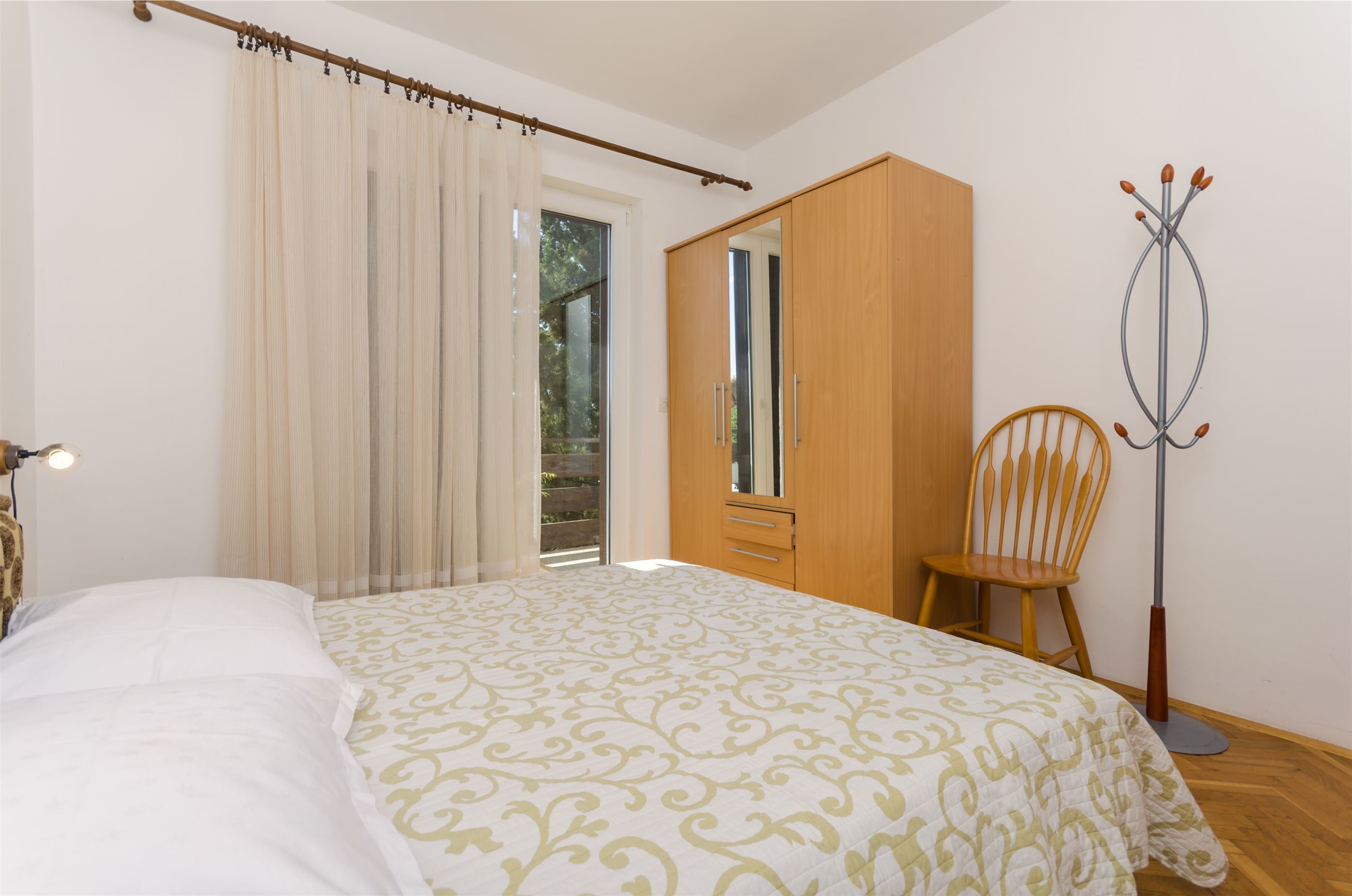 A bedroom with a bed, a wooden wardrobe, a chair, and a coat rack.