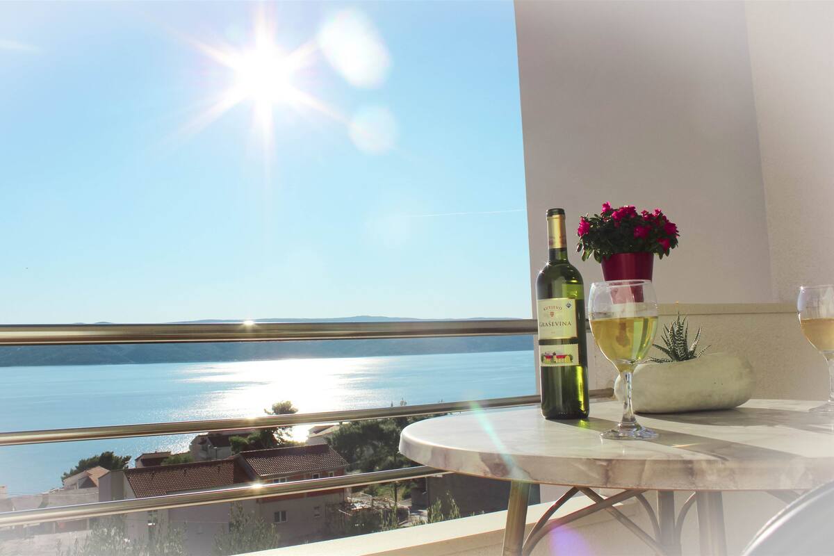A balcony with a view of the sea, a bottle of wine, a glass, and a potted plant.