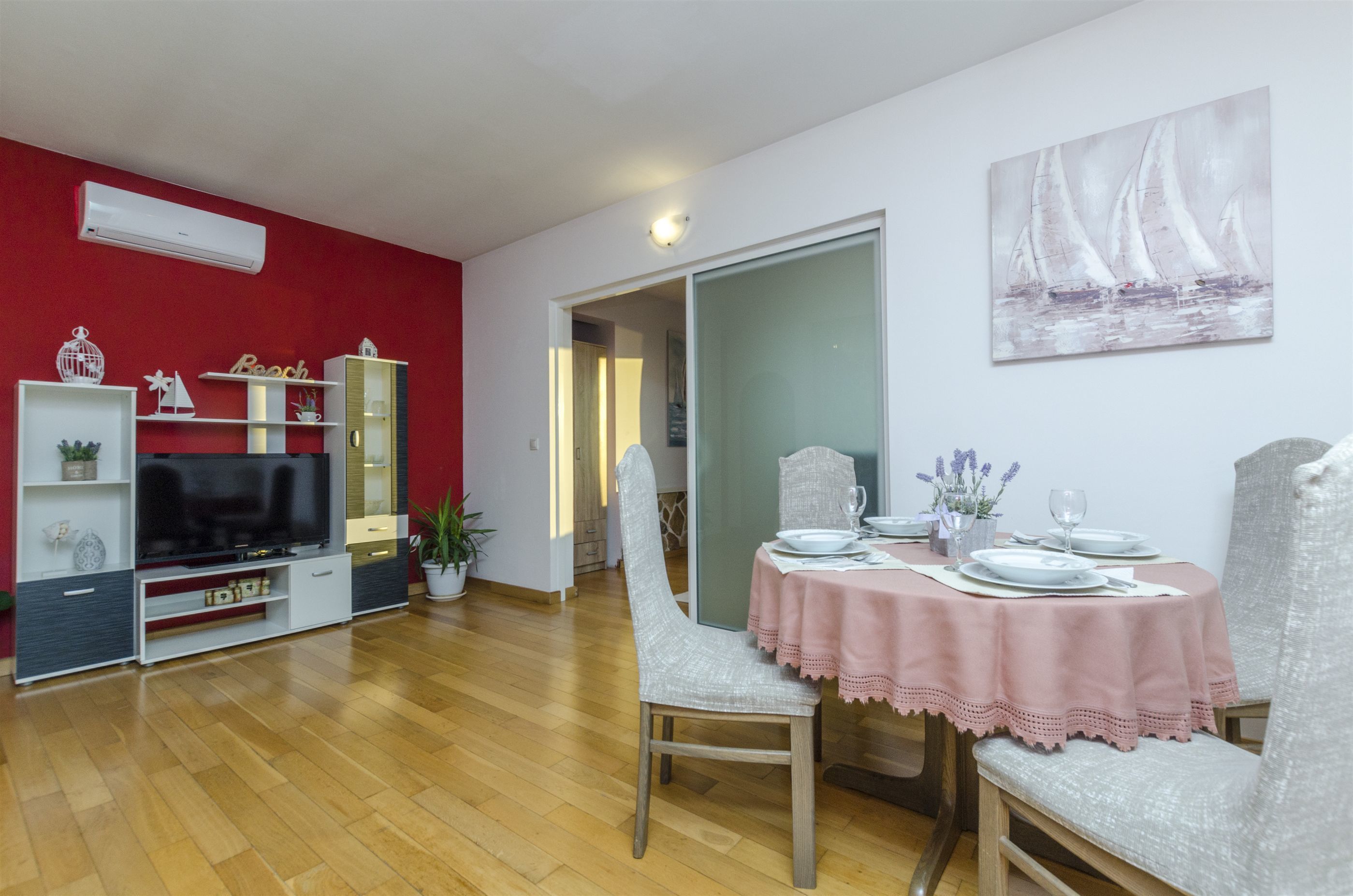 A dining area with a table set for four, a television in the living room, and a red accent wall.