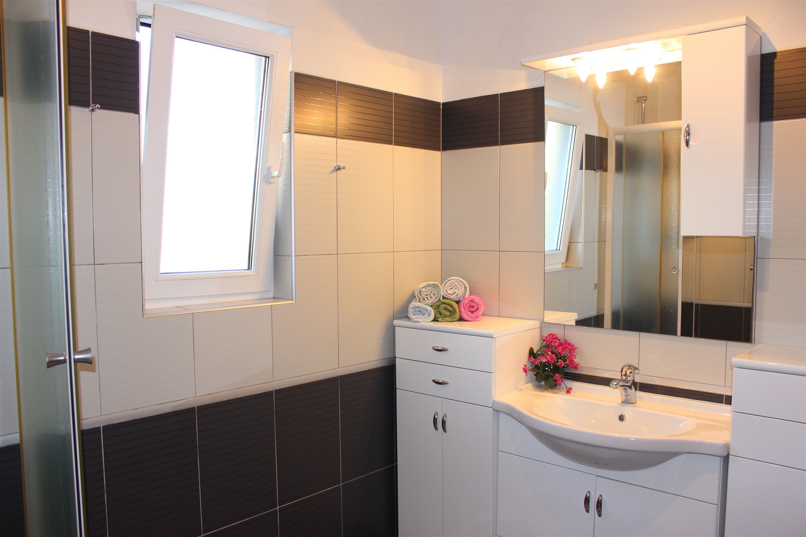 A bathroom with a white sink, a mirror, and a window.