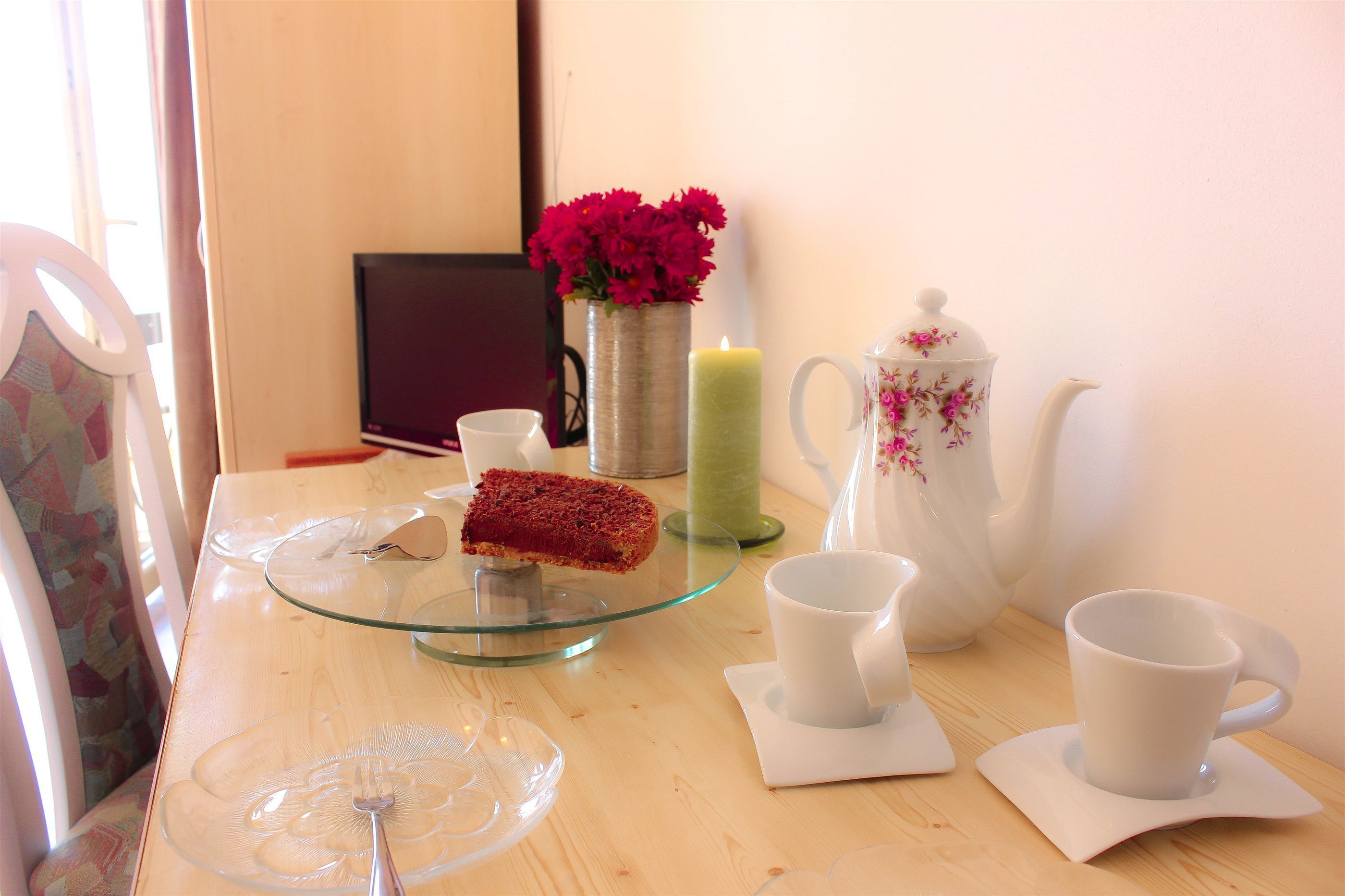 A table with a slice of cake, a candle, a teapot, and two cups.