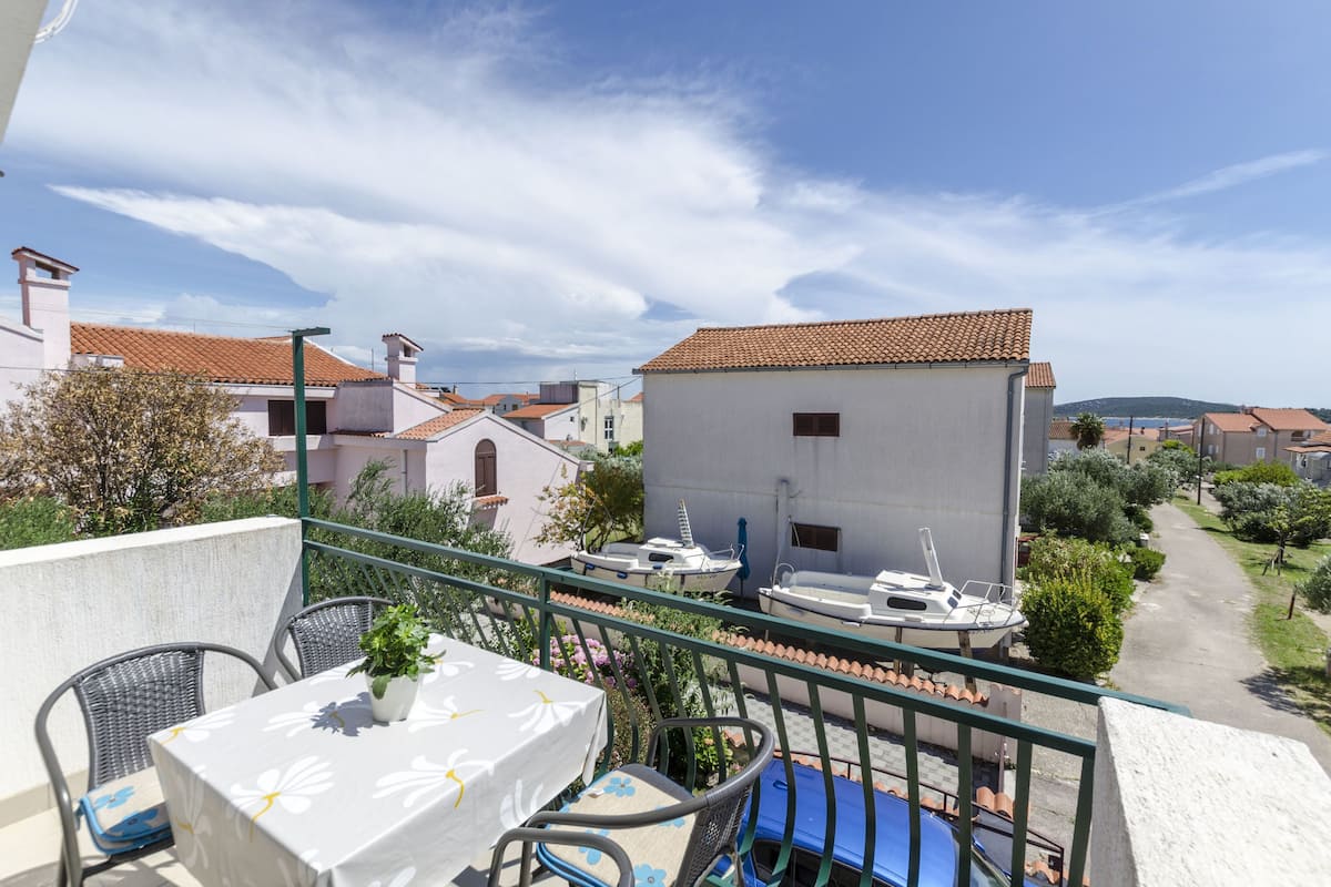 Uma varanda com mesa e cadeiras, com vista para uma área residencial com casas e céu claro.