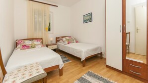 A bedroom with two beds, a wardrobe, a bedside table, a mirror, and a window with curtains. - Apartments Srdan (Rogoznica)