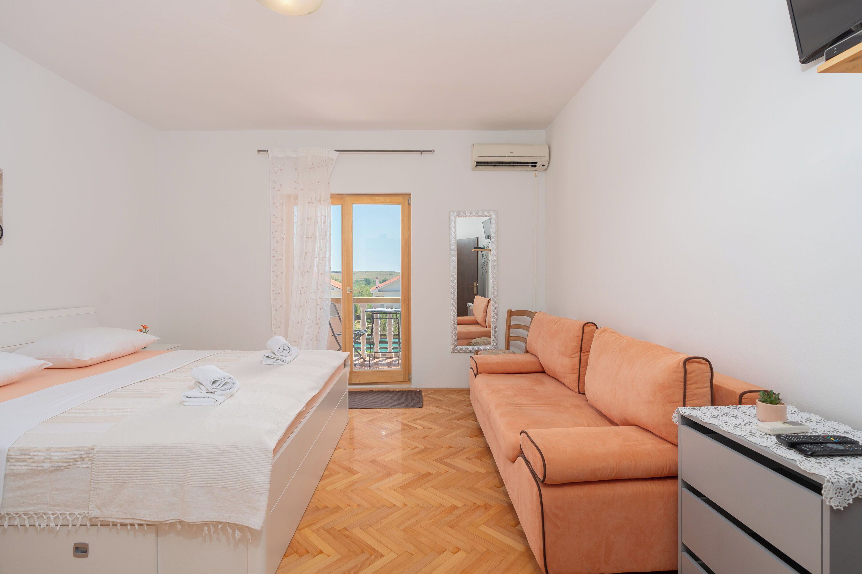 A bedroom with a bed, a sofa, a small table, and a balcony with a view.