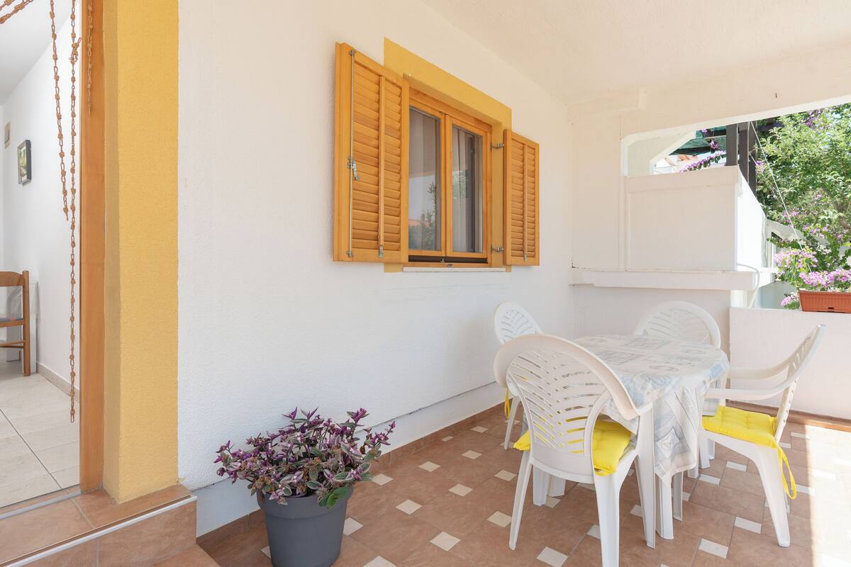 A balcony with a table and chairs, a potted plant, and a window with wooden shutters.