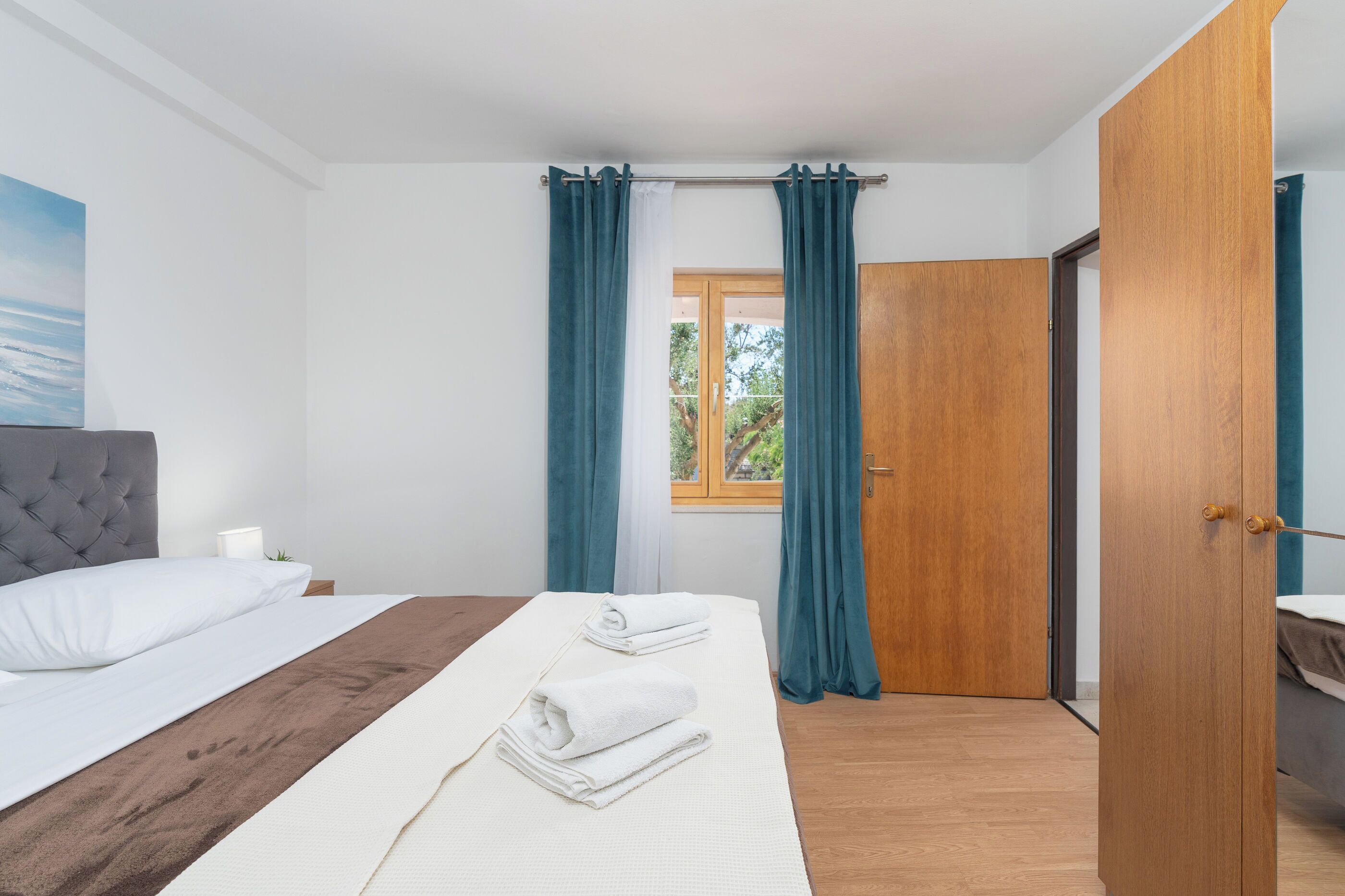A bedroom with a bed, a nightstand, a window with curtains, and a wooden door.