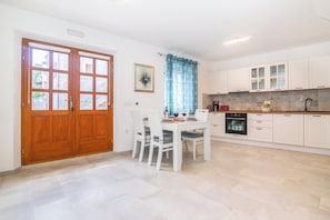 Una cocina con armarios blancos, una mesa de comedor con sillas y una puerta de madera.