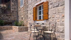 A stone building with a stone patio, a table with chairs, and a window with wooden shutters. - House Tia (Vrboska)