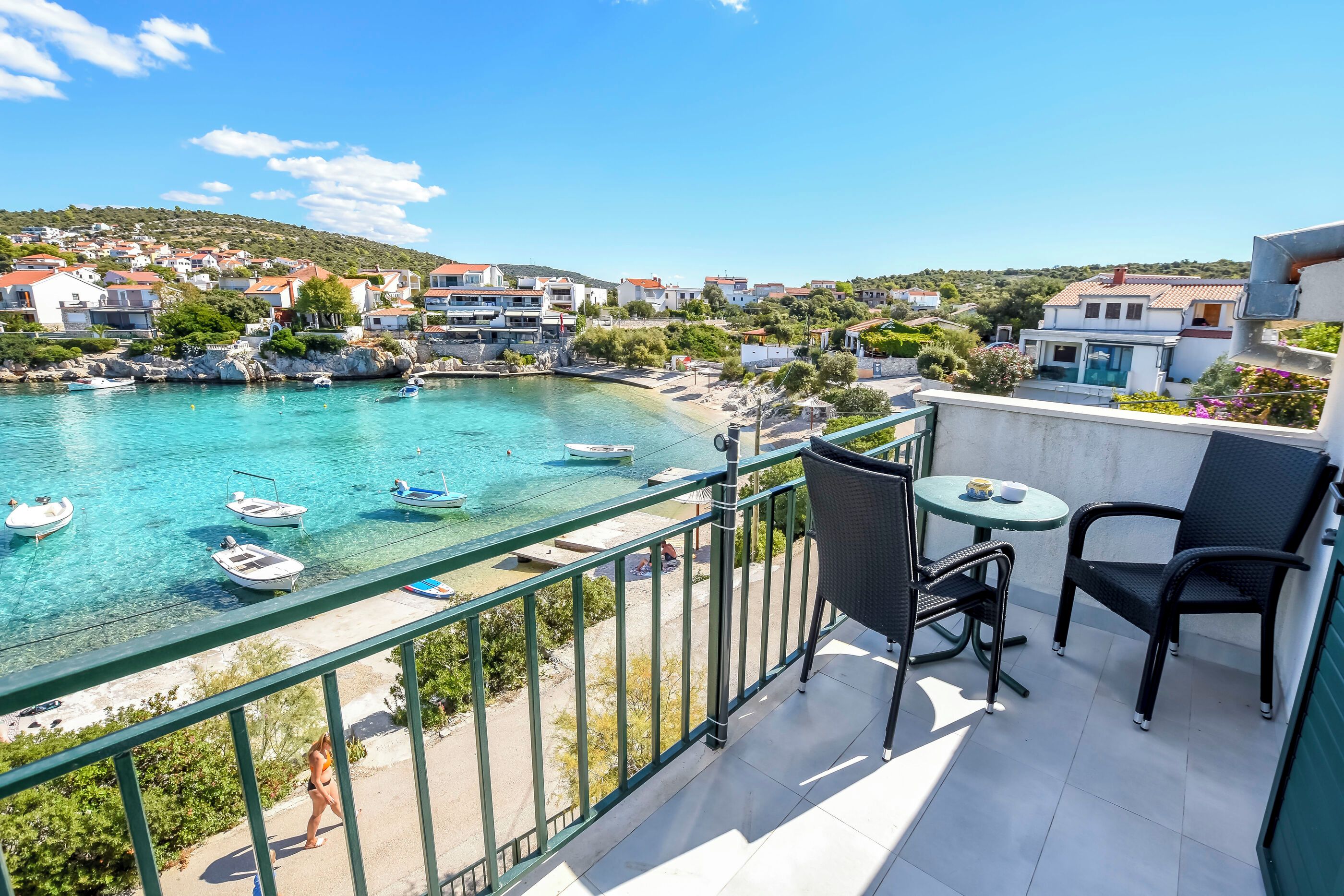 A balcony with a view of a coastal town, a pool, and a table with chairs.