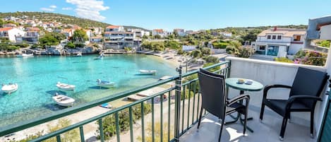 A balcony with a view of a coastal town, a pool, and a table with chairs.