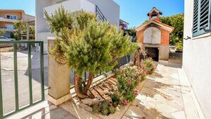 A modern building with a white facade, a small brick structure with a chimney, and a garden with various plants and flowers. - Apartments Sanda (Kanica)