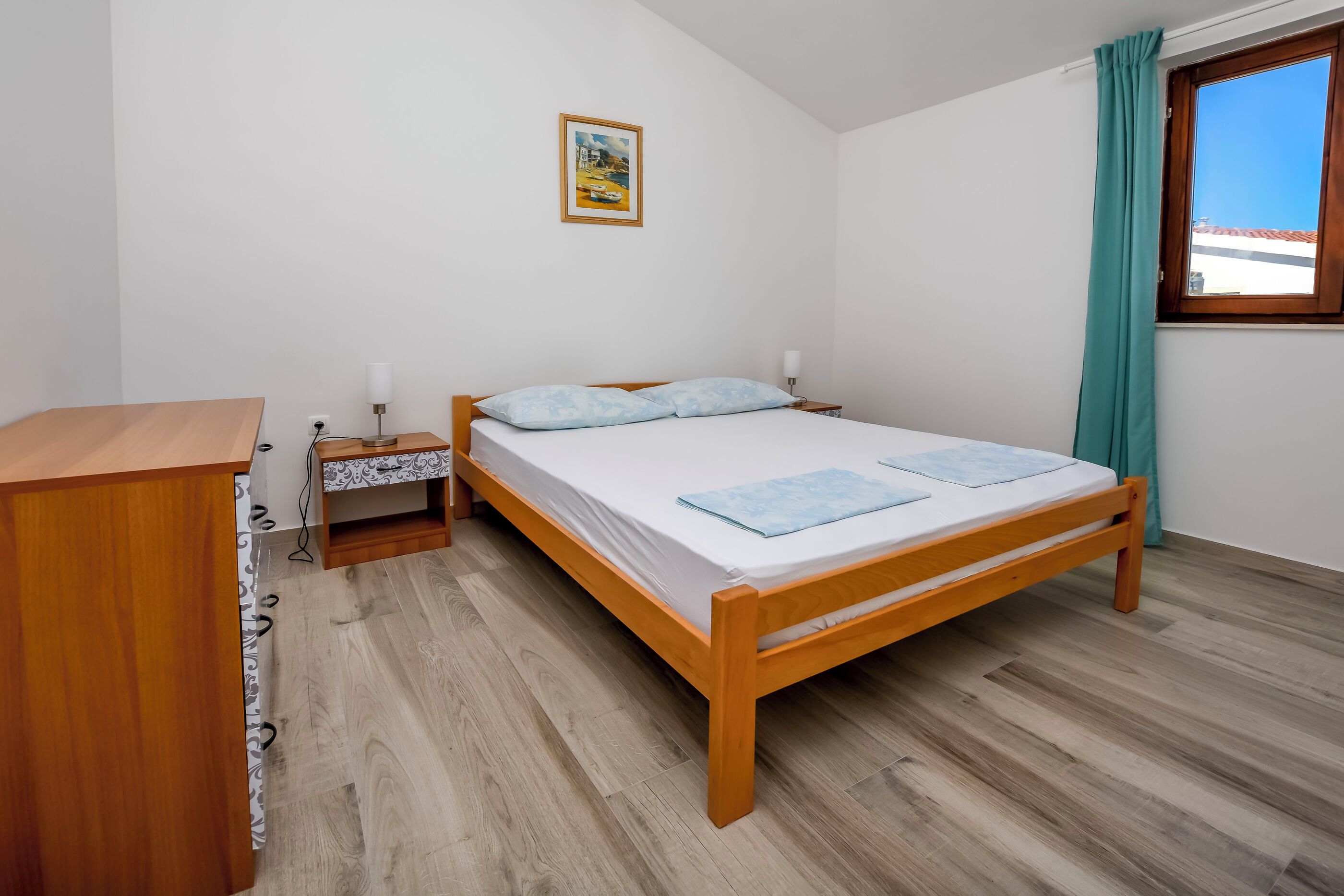 Un dormitorio con una cama de madera, una mesita de noche, un escritorio y una ventana con cortinas.