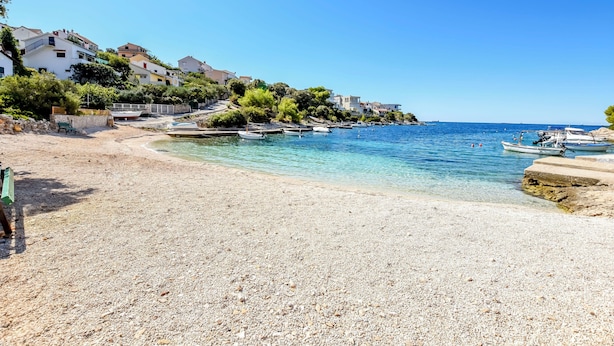 A pebble beach with boats, clear water, and buildings on a hillside. - Apartments Sanda (Kanica)