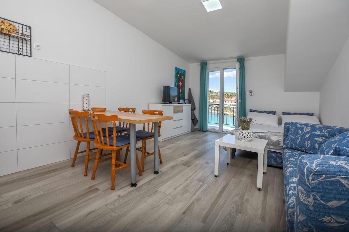 A modern, compact living space with a dining area, a sofa, and a balcony with a view.