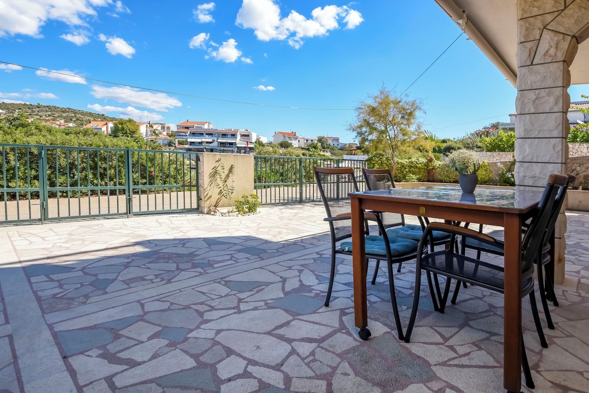 A patio with a table and chairs, a stone floor, and a view of houses in the background.