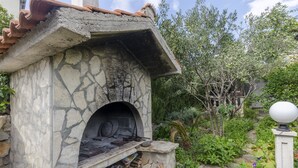 A stone-built outdoor oven with a rustic design, surrounded by lush greenery and a white spherical light fixture. - Apartments Miodrag (Stupin Celine)