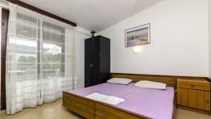 A bedroom with a bed, wooden headboard, a nightstand, a wardrobe, a window with sheer curtains, and a wall-mounted picture. - Apartments Miodrag (Stupin Celine)