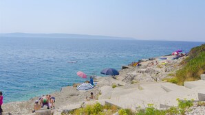 A coastal beach scene with people, umbrellas, and a clear view of the sea. - Apartments Sanja (Okrug Gornji)