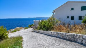 A coastal road leading to a white building with green shutters, overlooking the sea. - Apartments Sanja (Okrug Gornji)