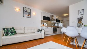 A modern living room with a white sofa, a coffee table, and a dining area with white chairs. - Apartments Sanja (Okrug Gornji)