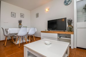 A modern living room with a dining area, white furniture, a flat-screen TV, and decorative vases.