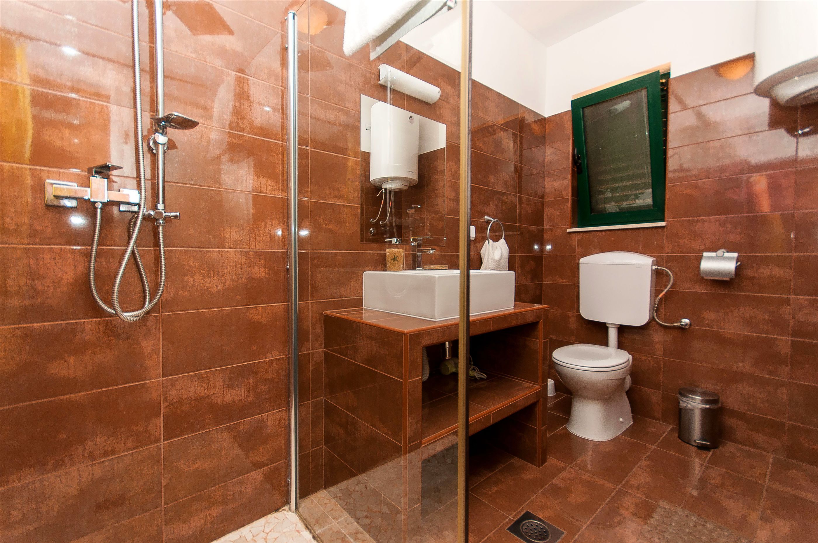 Une salle de bain avec une douche à parois de verre, un lavabo avec un miroir, des toilettes et une poubelle.