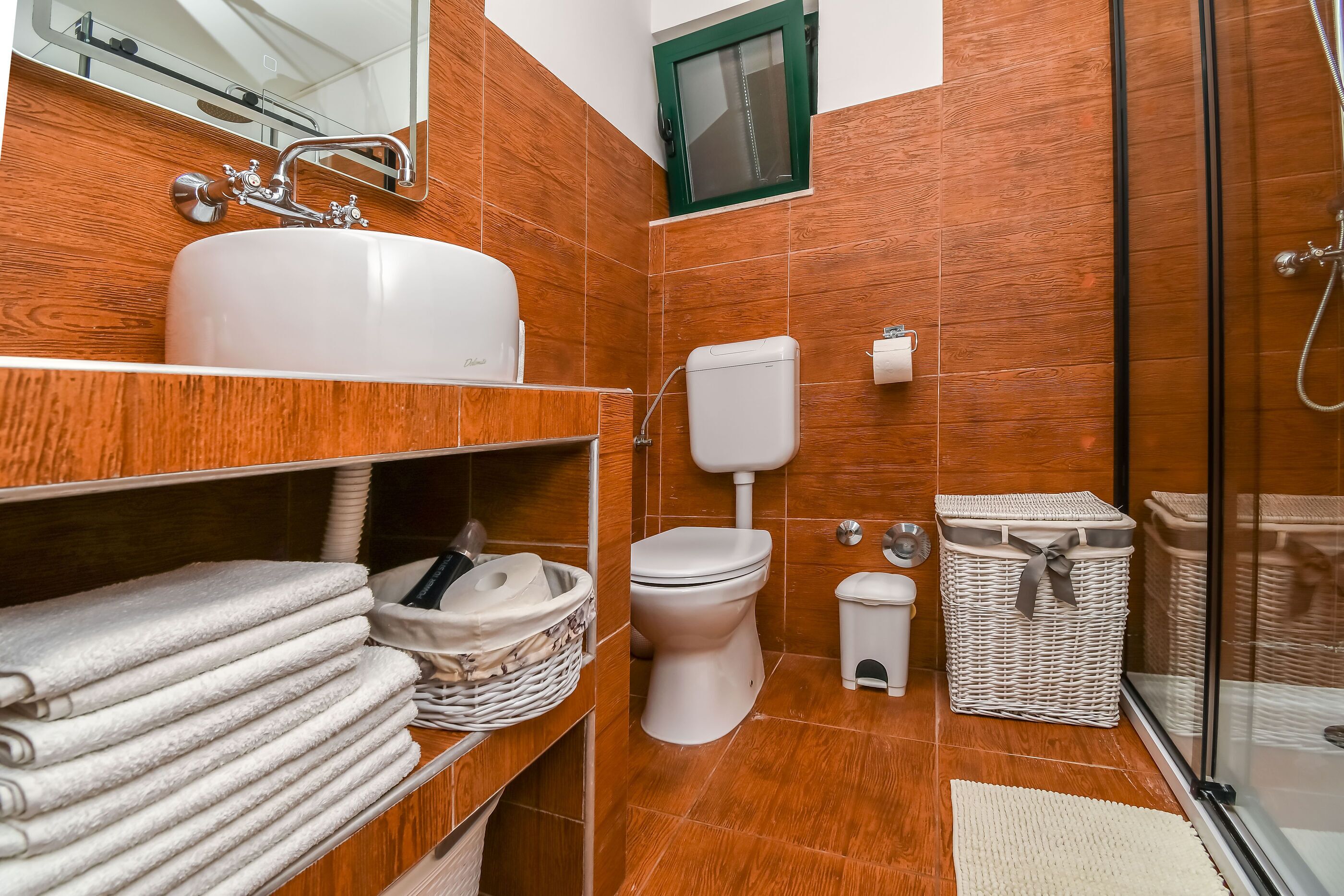 Un baño con lavamanos, inodoro y ducha blancos. Hay toallas y cestas en estantes.