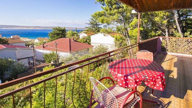 A balcony with a red polka dot tablecloth, a metal chair, and a view of the sea and houses. - Apartments Pavlina (Starigrad - Paklenica)